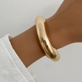 Close-up of a wide polished gold bangle bracelet styled with a white linen sleeve - Gold (02667)