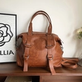 Bolso de mano clásico en cuero marrón con hebillas metálicas en un estante - Marrón Amarillento