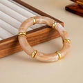 Close-up of marble resin tube bracelet with gold metal rings on a beige display - Milk Tea Color (03005)