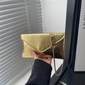 Detailed view of golden envelope clutch featuring water ripple texture and chain strap - Gold