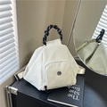 Minimalist cream triangular backpack with woven handle on a black cabinet in a stylish room - White