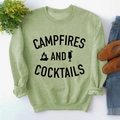 Flat lay of light green sweatshirt with CAMPFIRES AND COCKTAILS print and soft knit fabric - S / Olive Green Sweatshirt (Black Font)
