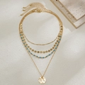 Détail de colliers dorés superposés avec perles bleues et pendentif rond à effet martelé - Style Multicouche Perles Bleu Ciel Pendentif Rond Martelé (05312)