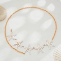 Detail of gold starfish body chain with white enamel charms on beach sand background - Gold+White