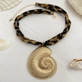 Großer goldener Schneckenanhänger an einer Stoffkette mit Leopardenmuster auf feinem Sand - Goldene Nautilusmodell (07101)