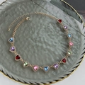 Detalle de collar de corazón colorido con cadena dorada y cristales en bandeja de vidrio - Dorado