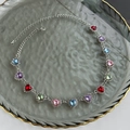 Detalle de collar de corazón plateado con pedrería colorida en bandeja de vidrio - Plateado