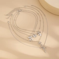 Detalle de 5 collares plateados con colgantes de lazo sobre fondo beige natural - Estilo Mariposa/Estrella (05977) / Plateado