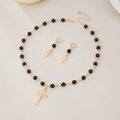 Detail of gold cross pendant necklace and beaded earrings set on beige background - Gold