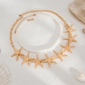 Detail of layered ocean style necklaces with golden starfish charms and pearls on white sand - Gold-06175