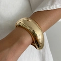 Close-up of a wide polished gold bangle with high gloss finish and smooth curves - Gold