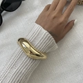 Detailed close-up of a chunky wavy gold cuff bracelet worn over a white knit sweater - Gold