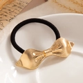 Elegant black hair tie with gold textured metal bow ornament on white porcelain plate - Gold Ribbed Bowknot (0078)