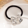Elegant black elastic hair tie with silver metallic bow charm on white plate - Silver Polished Bowknot (0098)