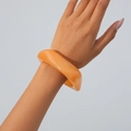 Close-up of translucent orange acrylic bangle with a glossy finish on wrist - Orange