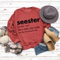 Detailed flat lay of brick red sweatshirt featuring Seester print on white wood background - S / Red (Black Font)