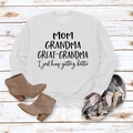 Platte lay van een witte MOM GRANDMA GREAT-sweater met laarzen en geruite sjaal - S / Wit (Zwart Lettertype)