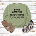 Mise à plat du sweat à col rond vert clair avec texte MOM sur un sol en bois blanc - Vert Olive (Police Noire)