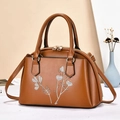 Detail of caramel crossbody bag with white leaf embroidery and gold hardware accents - Earthy Yellow
