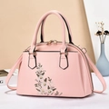 Pink matte leather handbag with floral embroidery and gold hardware in a scenic setting - Pink