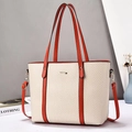 Close-up of beige herringbone tote bag with orange leather handles and gold hardware logo - Red