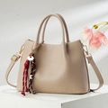 Detail of beige lychee leather handbag with braided key charm on white pedestal - Light Khaki