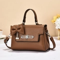 Classic brown pebble leather handbag with bow and pearl detail on a desk - Earthy Yellow