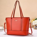 Close-up of orange tote bag featuring silver metal bar and detachable shoulder strap - Red