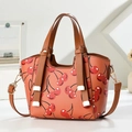 Minimalist coral dumpling bag with cherry print and brown straps shown in lifestyle setting - Earthy Yellow