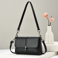Classic black pebbled leather crossbody bag with metal buckle on a marble pedestal - Black