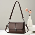 Brown faux leather crossbody bag with lychee texture and metallic clasp on a stone display - Coffee