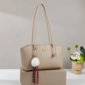 Minimalist beige tote bag with gold logo and white pom-pom charm on a display stand - Khaki
