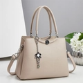 Close-up of beige lychee grain handbag with camellia logo and floral crystal pendant - Apricot