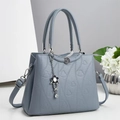 Dettaglio della borsa tote in pelle blu con goffratura a cuore e ciondolo a fiore - Blu