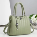 Close-up of sage green leather handbag with floral metal charm and textured finish - Green