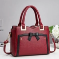 Close-up of red lychee texture handbag with black bow detail and gold hardware - Burgundy
