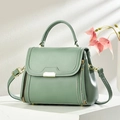 Sage green elegant leather handbag with top handle and gold metal trim on display stand - Green