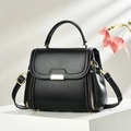 Detail of black crossbody bag with gold hardware, white stitching, and flap design - Black