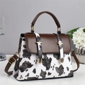 Detail of a cow print shoulder bag with brown leather accents and gold metal hardware - Black