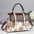 Chic cow print handbag with brown leather flap and gold hardware on a display table - Apricot
