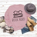 Rosa Sweatshirt mit Book Nerd Print kombiniert mit Jeans und Stiefeln auf Holzhintergrund - S / Rosa (Schwarzer Text)