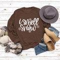 Flat lay of brown 'I smell Snow' sweatshirt with winter accessories on wood - S / Coffee (White Font)