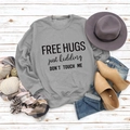 Flat lay of gray long sleeve sweatshirt with Free Hugs slogan on white wooden background - Grey Sweatshirt (Black Font)