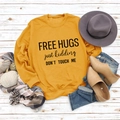 Flat lay of mustard yellow sweatshirt with Free Hugs slogan and autumn accessories - Yellow Sweatshirt (Black Font)