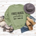 Flat lay of green sweatshirt with Free Hugs slogan and autumn accessories on wood - Olive Green Sweatshirt (Black Font)