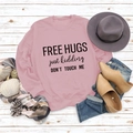 Flat lay of pink sweatshirt with Free Hugs slogan on white wood background - Pink Sweatshirt (Black Font)