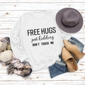 Flat lay of white sweatshirt with Free Hugs slogan print on white wood background - White Sweatshirt (Black Font)