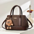 Detail of dark brown lychee leather handbag with vertical texture and plush ball charm - Coffee