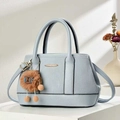 Light blue embossed leather handbag with top handles and a plush charm on a white pedestal - Light Blue