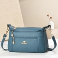 Detail van groenblauwe crossbodytas met lycheetextuur en gouden kangoeroelogo-hardware - Blauw